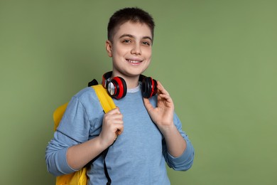 Photo of Teenage boy with headphones and backpack on green background