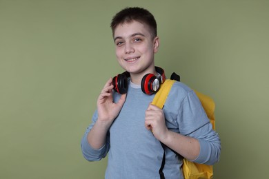 Photo of Teenage boy with headphones and backpack on olive background