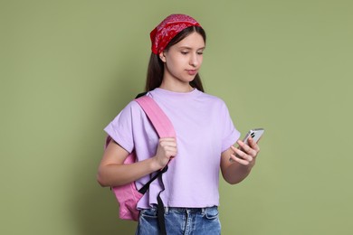 Photo of Teenage girl with smartphone and backpack on olive background