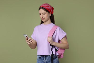 Teenage girl with smartphone and backpack on olive background