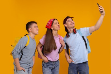 Photo of Happy students taking selfie on orange background