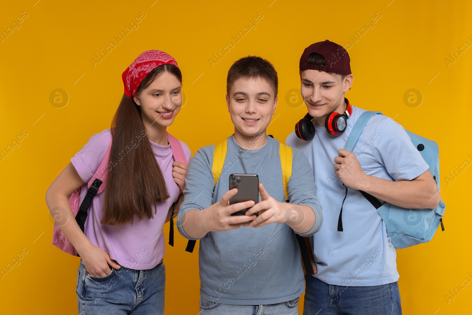 Photo of Student showing something on smartphone to his friends against orange background