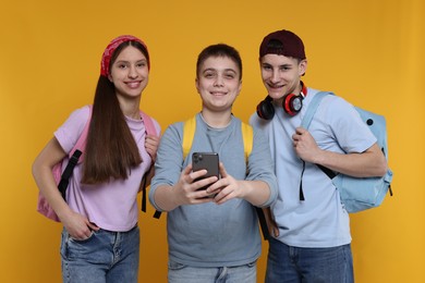 Photo of Student showing something on smartphone to his friends against orange background