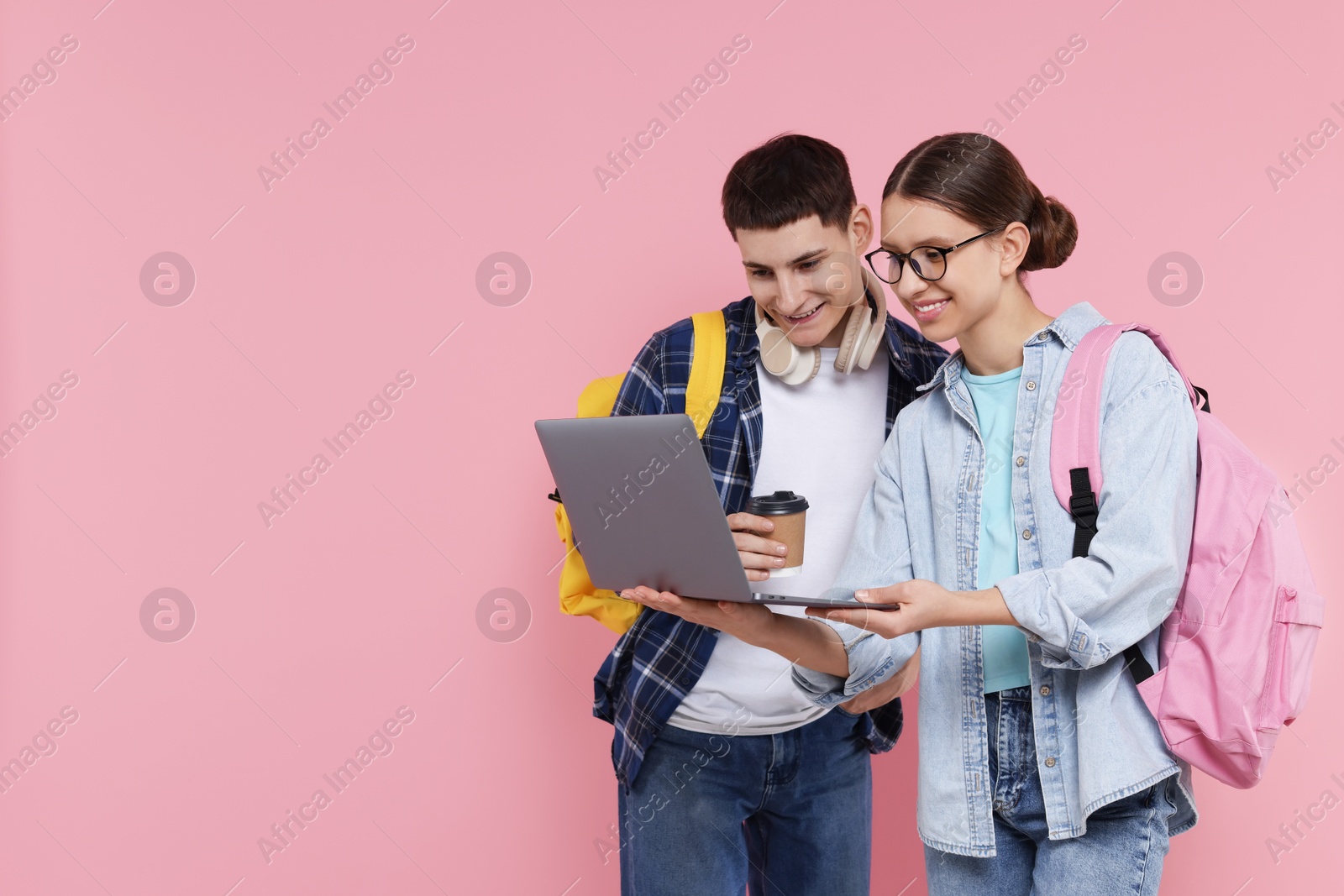 Photo of Teenage girl showing something on laptop to her friend against pink background, space for text