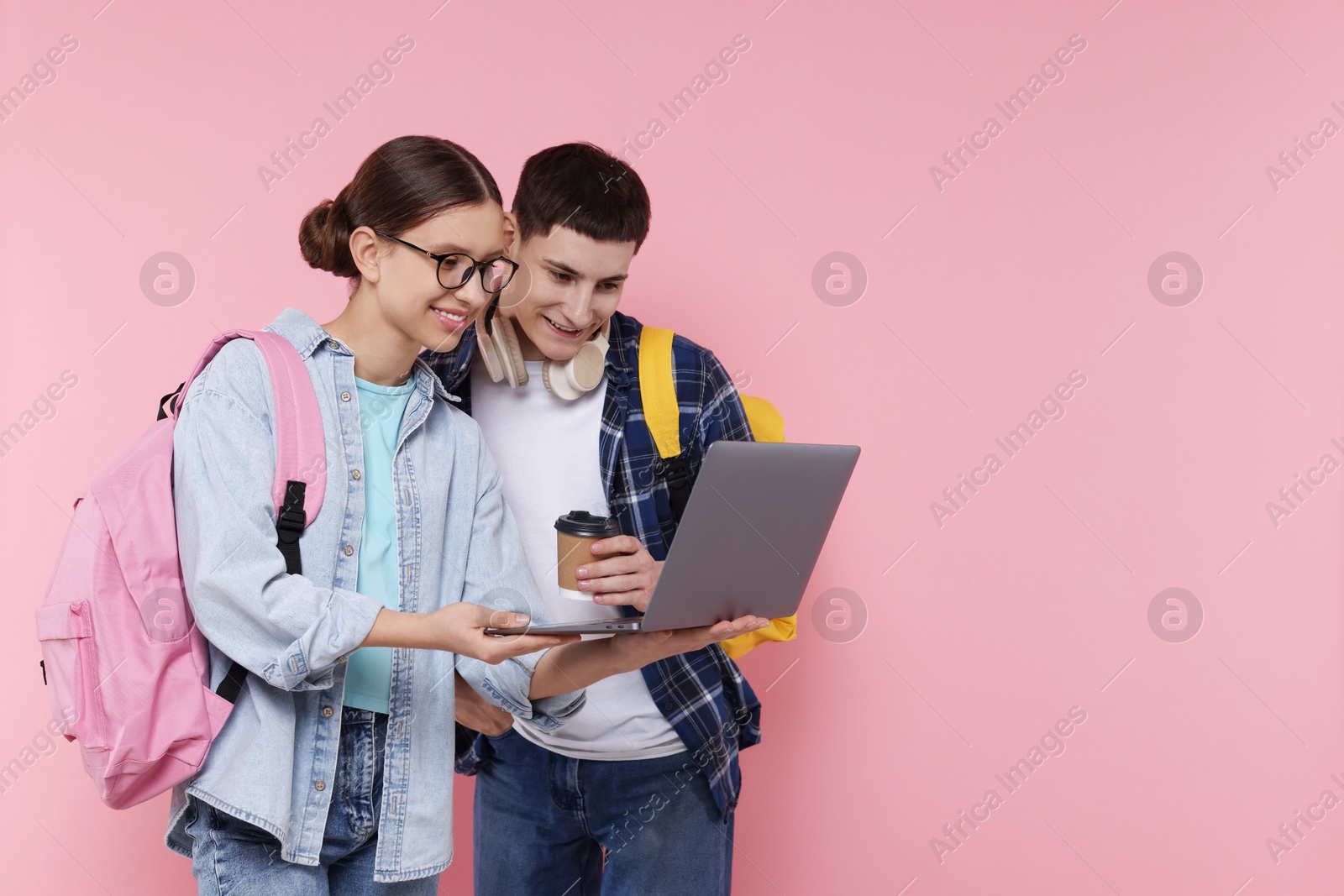 Photo of Teenage girl showing something on laptop to her friend against pink background, space for text