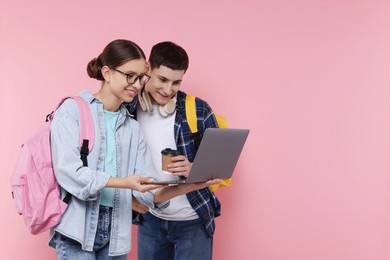 Teenage girl showing something on laptop to her friend against pink background, space for text