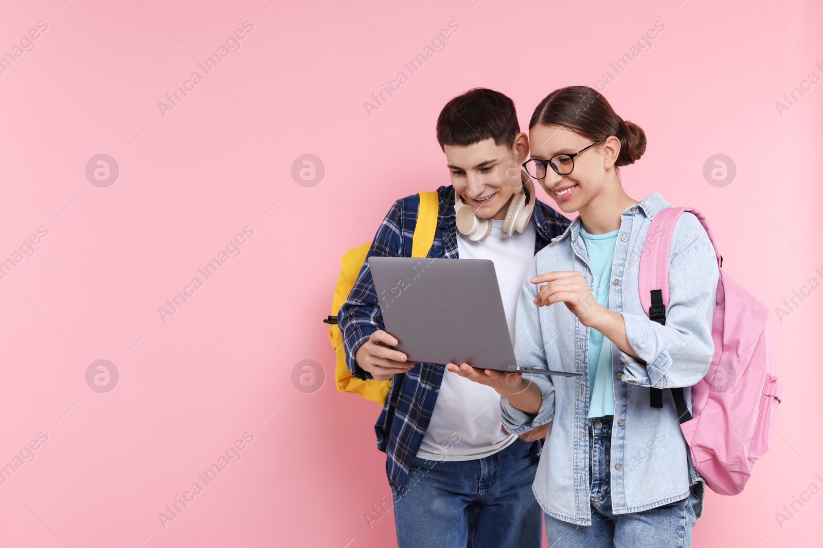 Photo of Teenage girl showing something on laptop to her friend against pink background, space for text