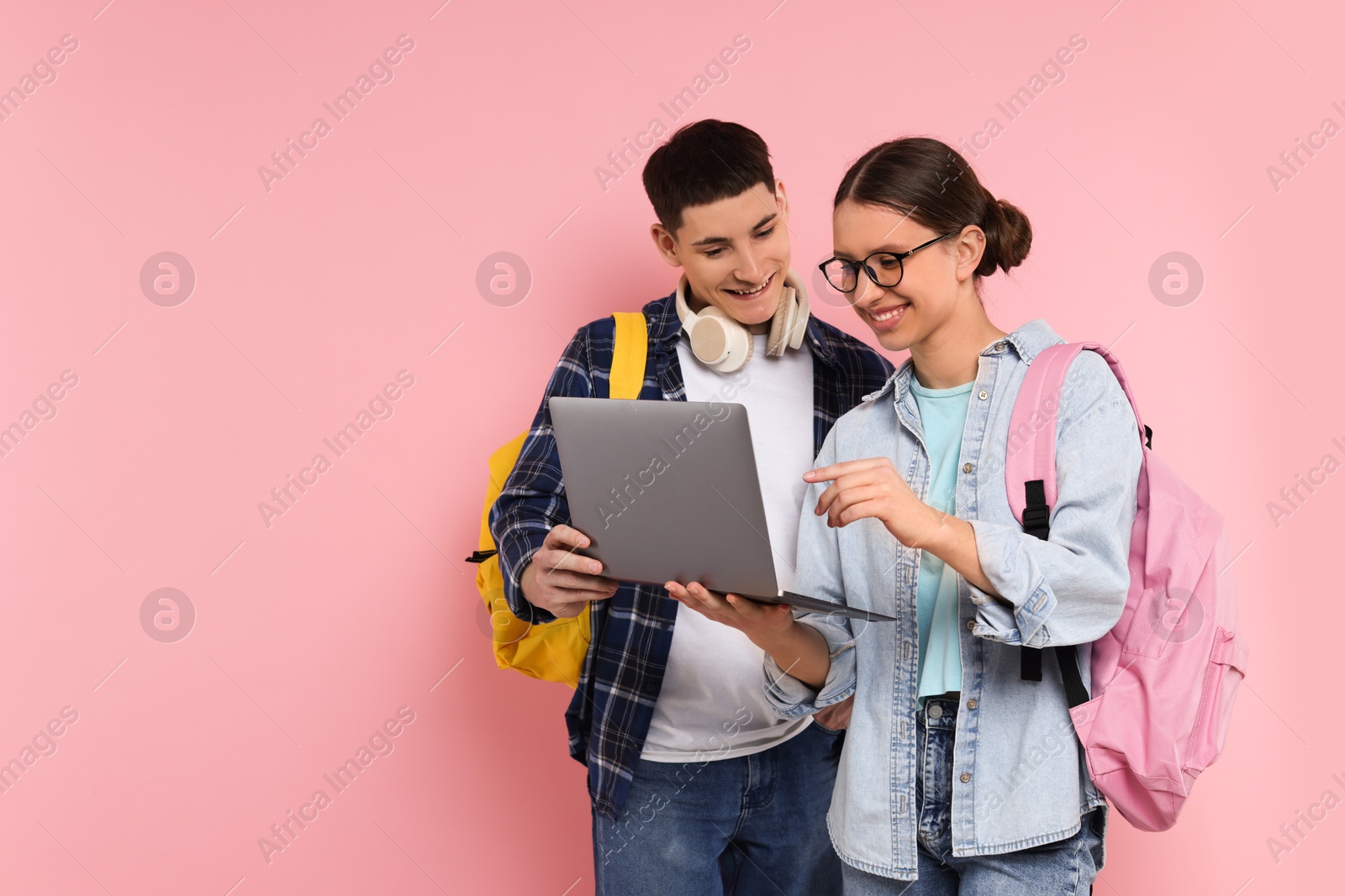 Photo of Teenage girl showing something on laptop to her friend against pink background, space for text