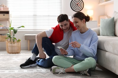 Photo of Teenage girl showing something on smartphone to her friend at home