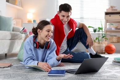 Students doing homework with laptop on floor at home