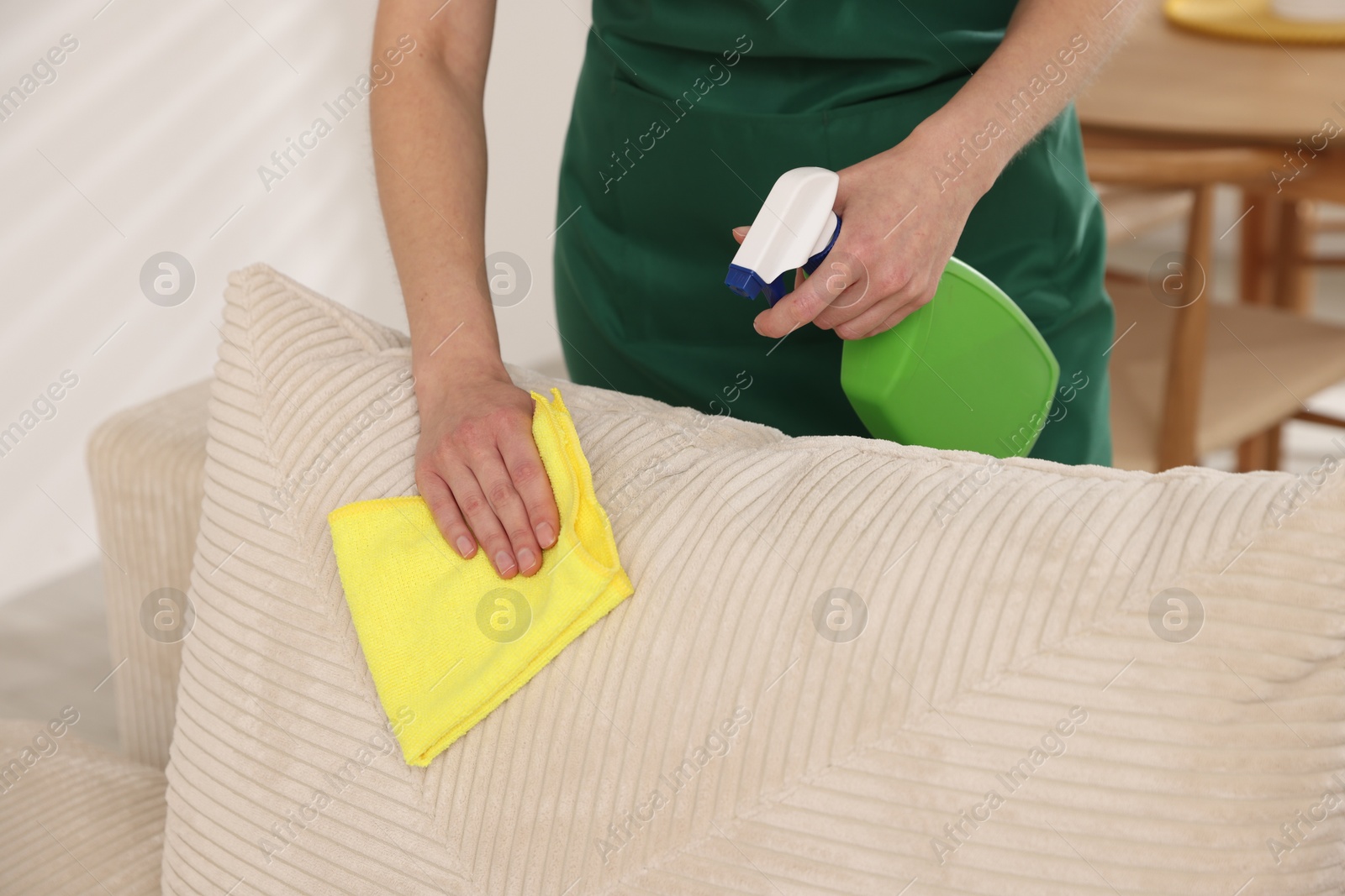 Photo of Janitor cleaning sofa with rag at home, closeup