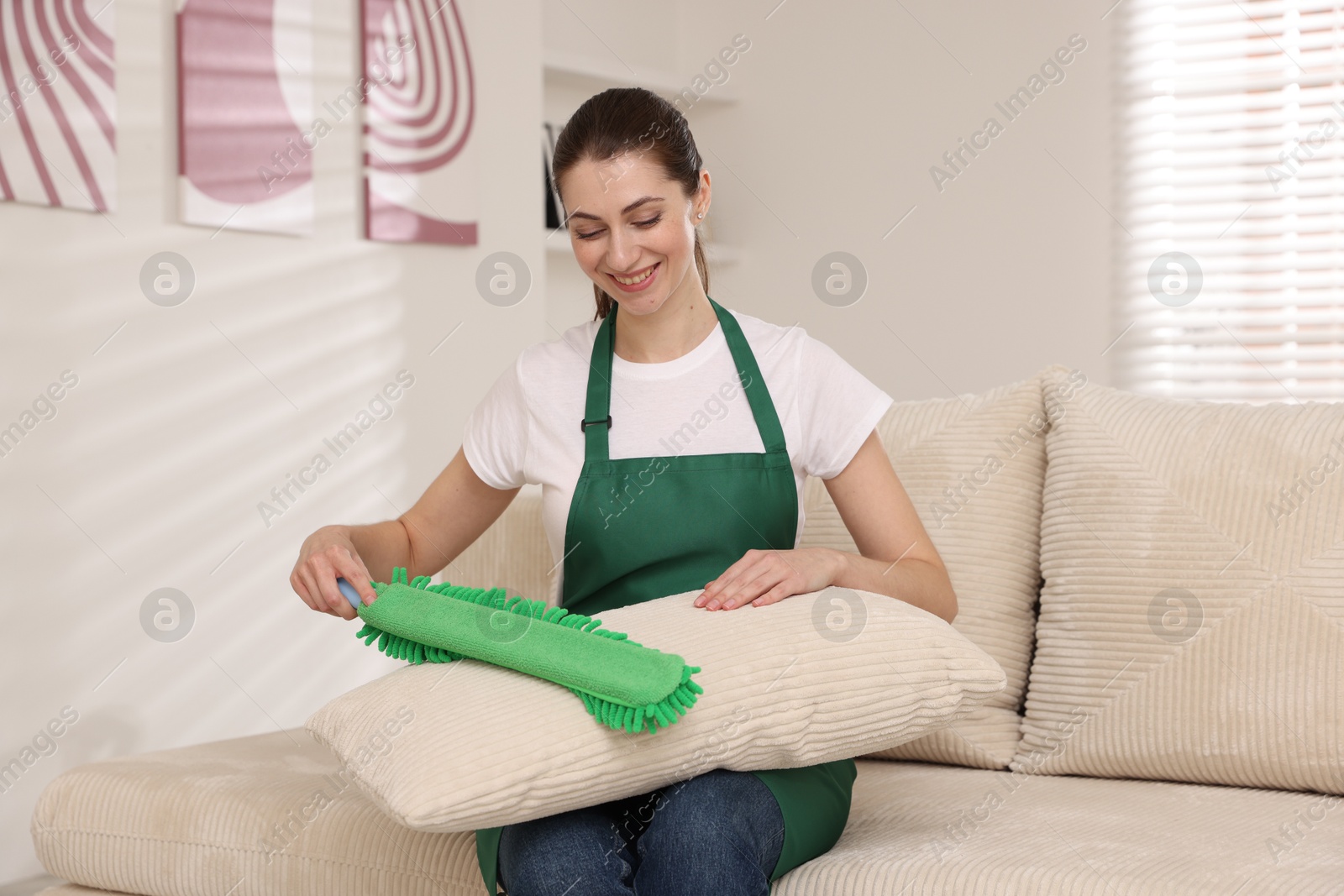 Photo of Janitor cleaning sofa cushion with duster at home