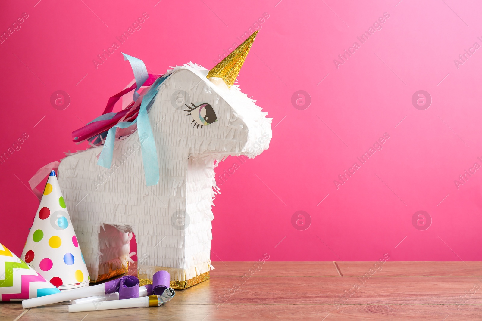 Photo of Beautiful pinata in shape of unicorn, party cones and blowers on wooden table against pink background. Space for text