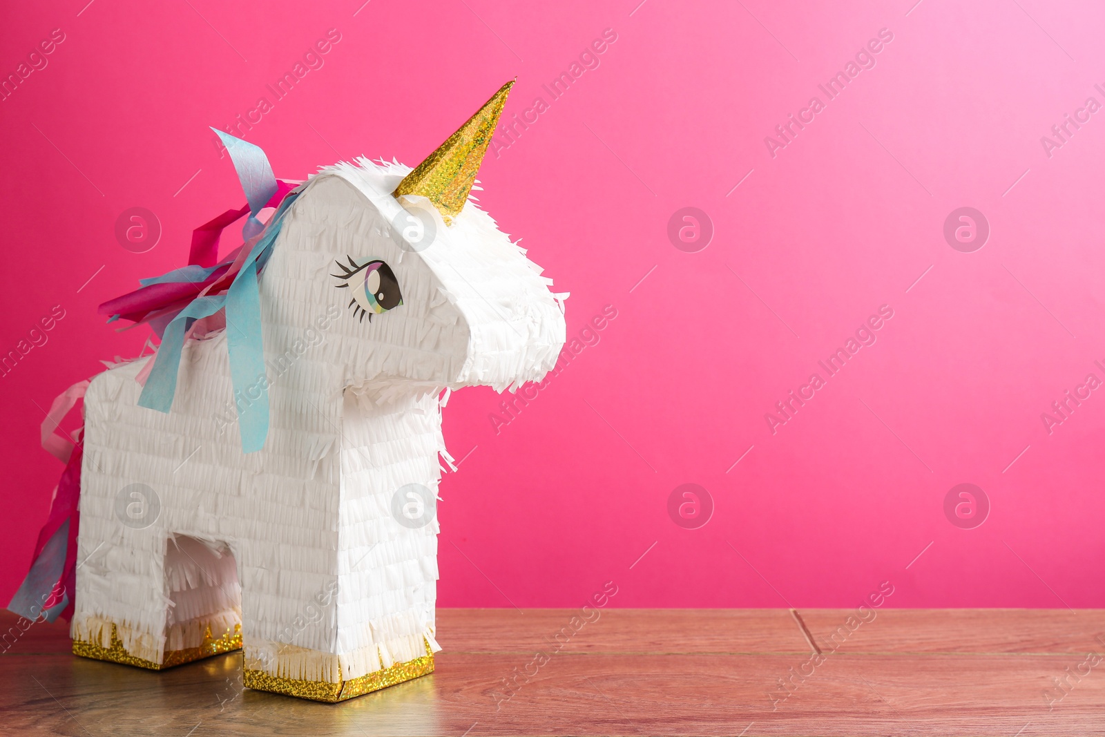 Photo of Beautiful pinata in shape of unicorn on wooden table against pink background. Space for text