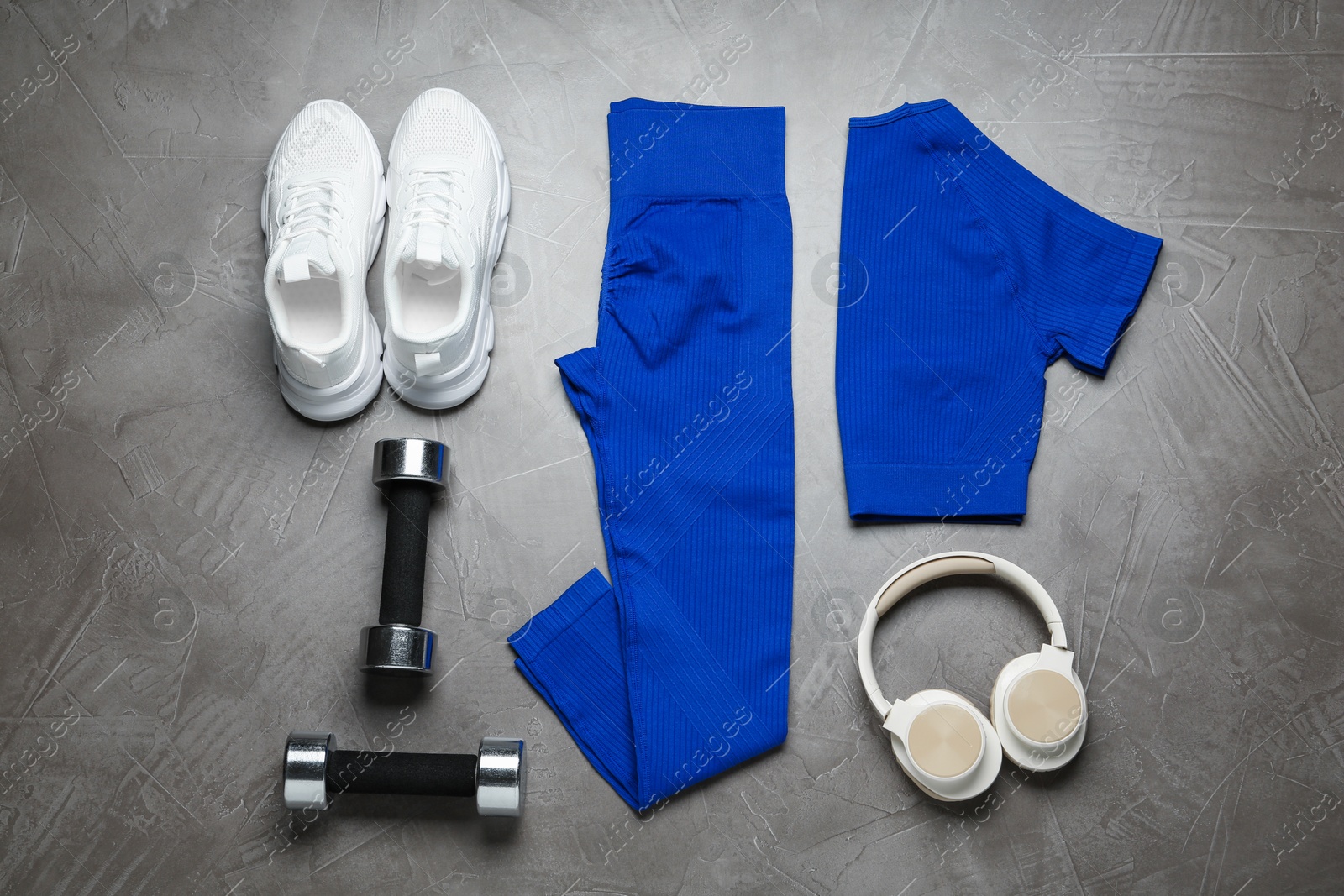 Photo of Blue sportswear, white sneakers, dumbbells and headphones on gray textured background, flat lay