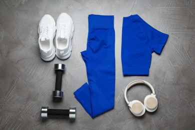 Photo of Blue sportswear, white sneakers, dumbbells and headphones on gray textured background, flat lay