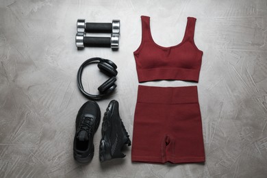 Photo of Brown sportswear, black sneakers, dumbbells and headphones on gray textured background, flat lay