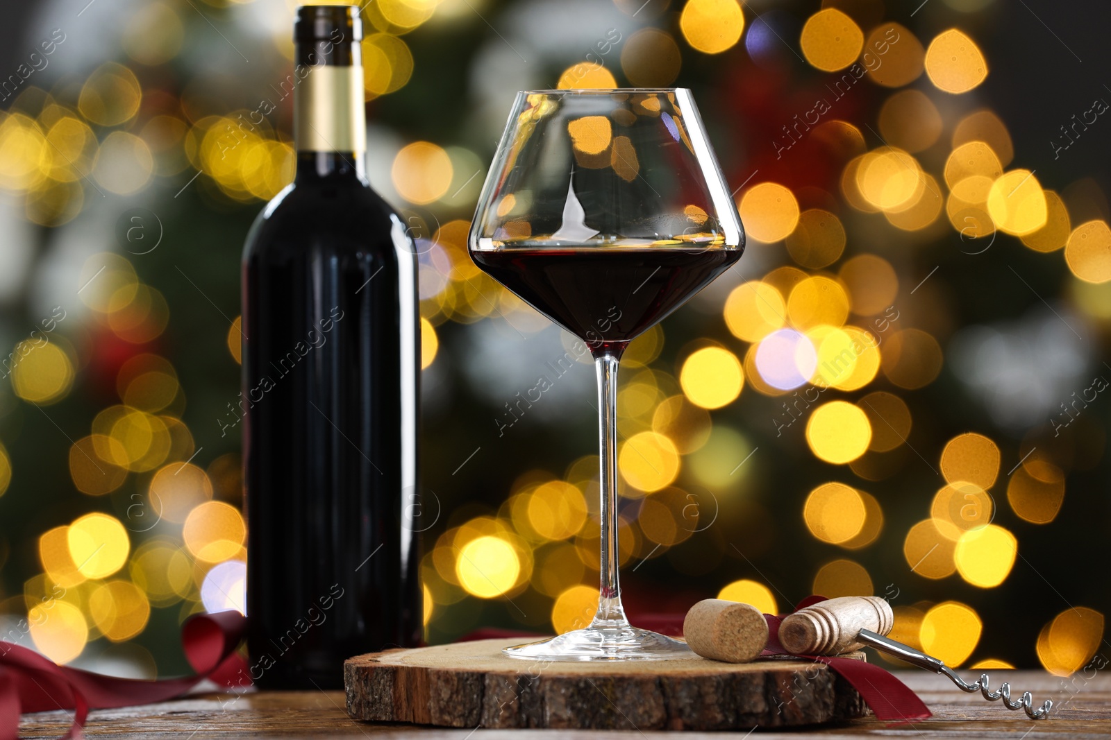 Photo of Red wine in glass, bottle and corkscrews on wooden table against blurred Christmas lights, closeup