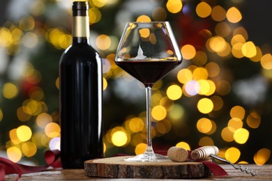 Photo of Red wine in glass, bottle and corkscrews on wooden table against blurred Christmas lights, closeup