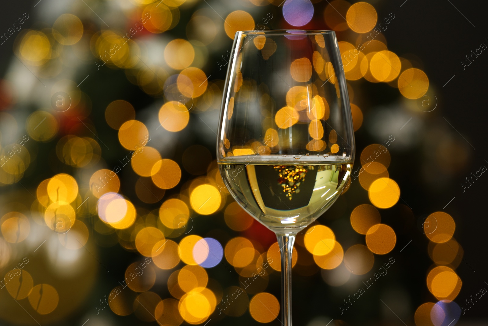 Photo of White wine in glass against blurred Christmas lights, closeup