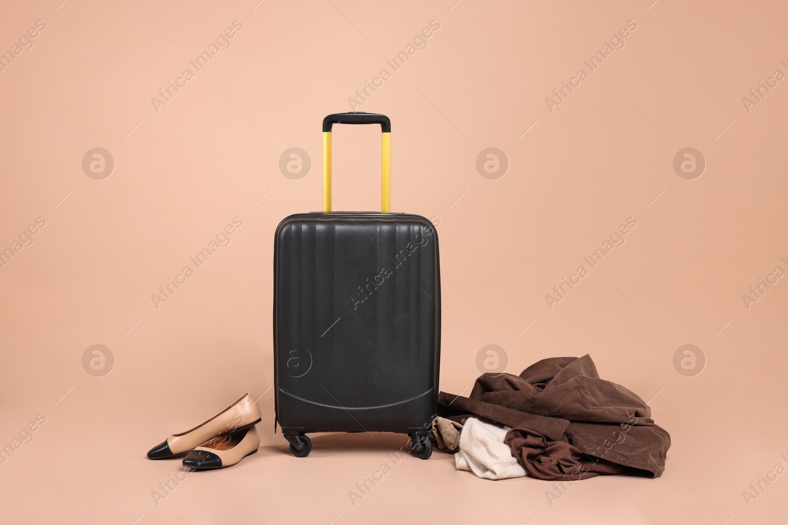 Photo of Suitcase, shoes and messy pile of clothes on beige background
