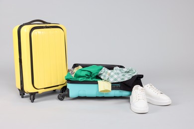 Photo of Suitcases with messy clothes and shoes on light background