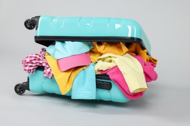 Photo of Packed suitcase full of clothes on light grey background