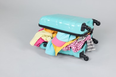 Photo of Packed suitcase full of clothes on light grey background