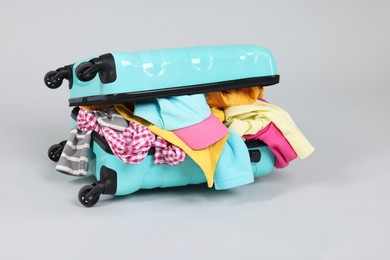 Photo of Packed suitcase full of clothes on light grey background