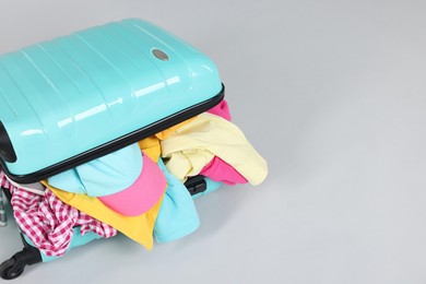 Photo of Packed suitcase full of clothes on light grey background, closeup. Space for text