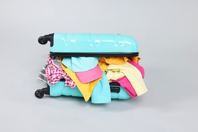 Photo of Packed suitcase full of clothes on light grey background