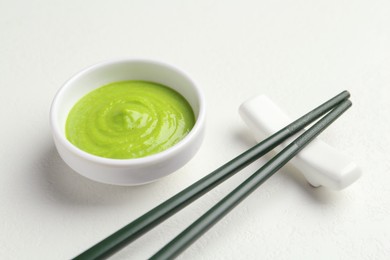 Photo of Hot wasabi paste in bowl and chopsticks on light textured table, closeup