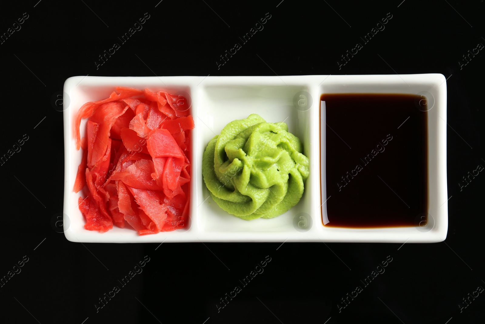 Photo of Hot wasabi paste, soy sauce and ginger on black background, top view