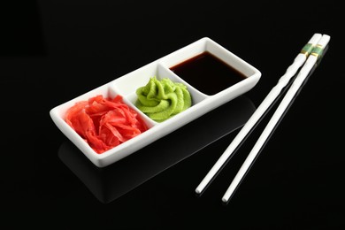 Photo of Hot wasabi paste, soy sauce, ginger and chopsticks on black mirror surface, closeup