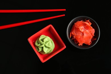 Photo of Hot wasabi paste, ginger and chopsticks on black background, flat lay