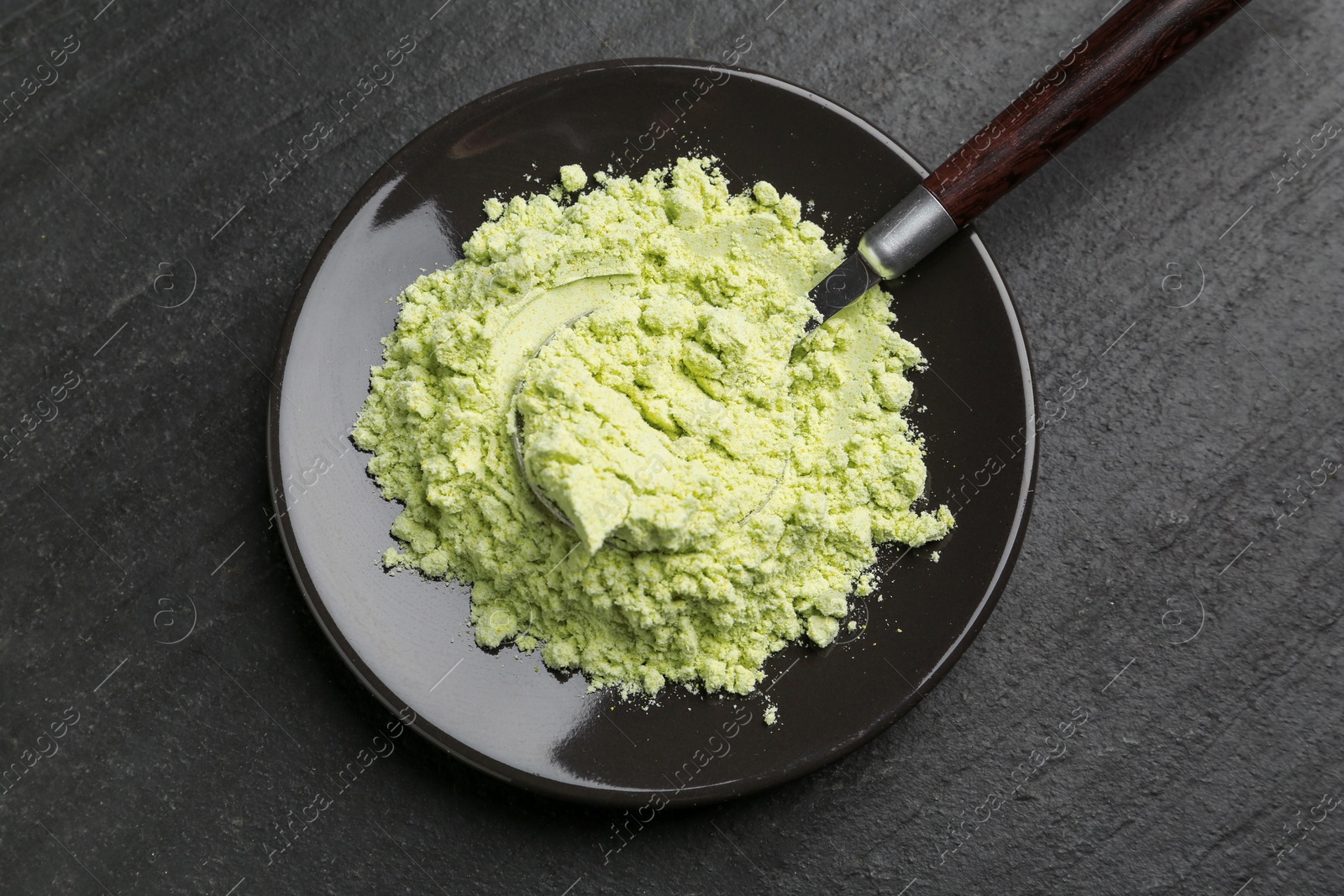 Photo of Plate with dry wasabi powder and spoon on dark textured table, top view