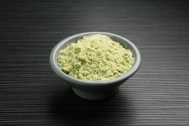 Photo of Wasabi powder in bowl on black textured table, closeup