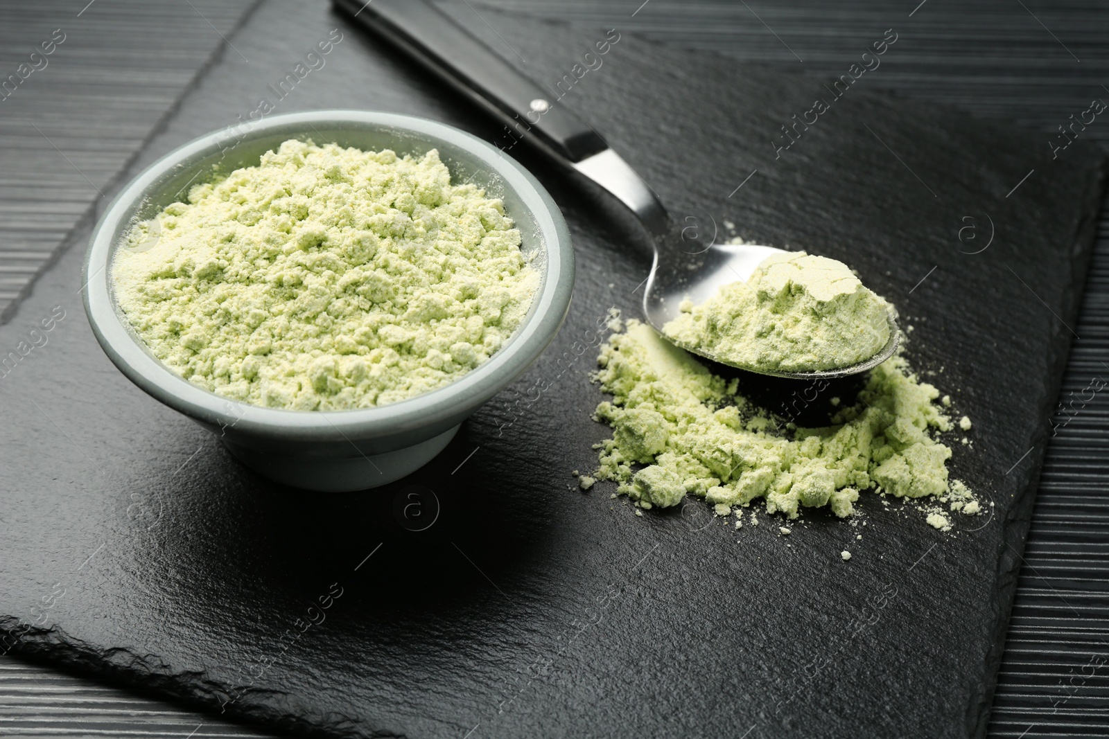 Photo of Dry wasabi powder and spoon on black textured table, closeup