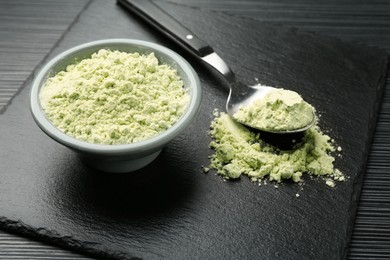 Photo of Dry wasabi powder and spoon on black textured table, closeup