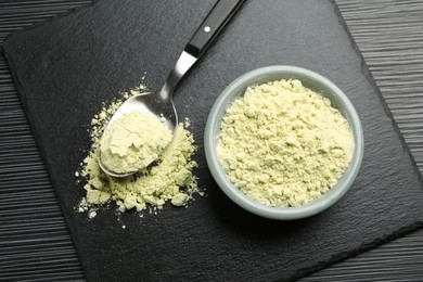 Photo of Dry wasabi powder and spoon on black textured table, top view