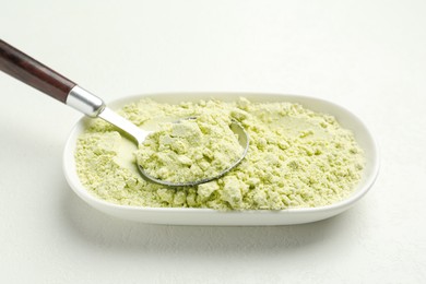 Photo of Dry wasabi powder and spoon on white textured table, closeup