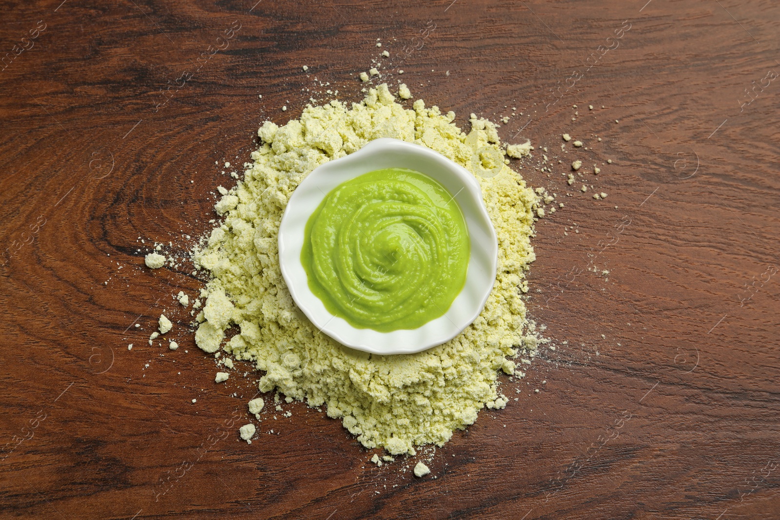 Photo of Pile of dry wasabi powder and bowl with paste on wooden table, top view