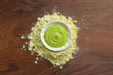 Photo of Pile of dry wasabi powder and bowl with paste on wooden table, top view