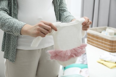 Photo of Pregnant woman with baby clothes at home, closeup