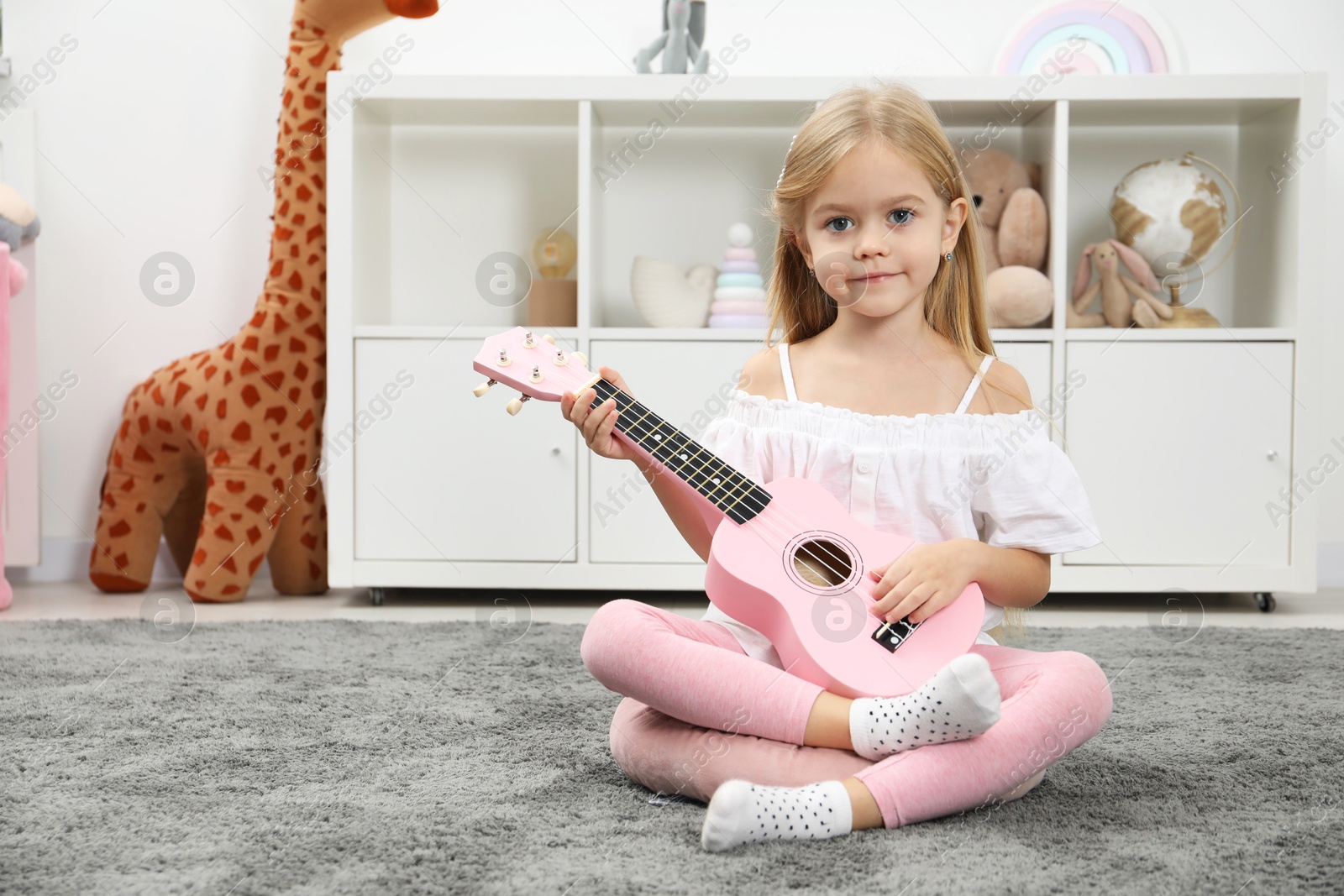 Photo of Little girl with pink ukulele at home