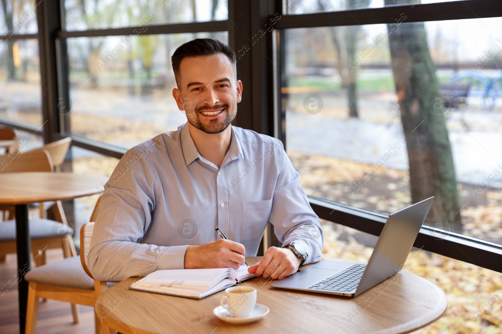 Photo of Man taking notes at table in cafe