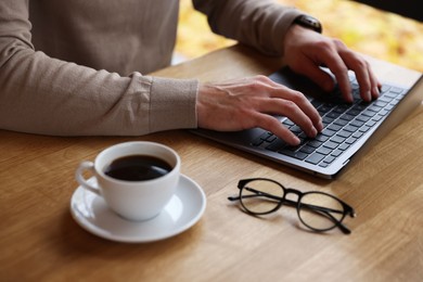 Photo of Man working on laptop at wooden table in cafe, closeup