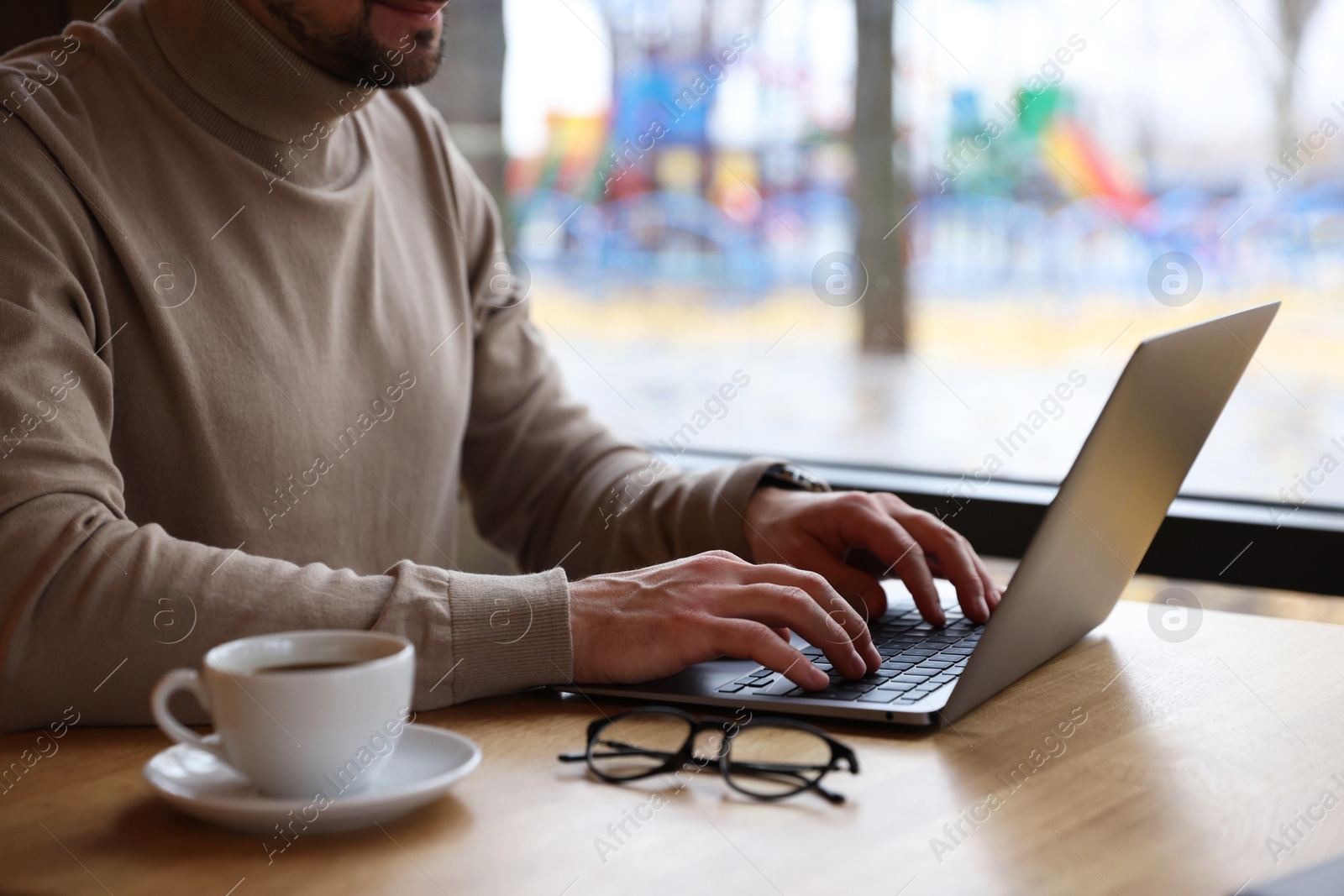 Photo of Man working on laptop at wooden table in cafe, closeup