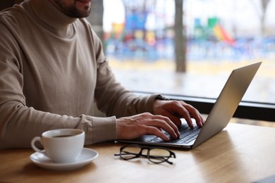 Photo of Man working on laptop at wooden table in cafe, closeup