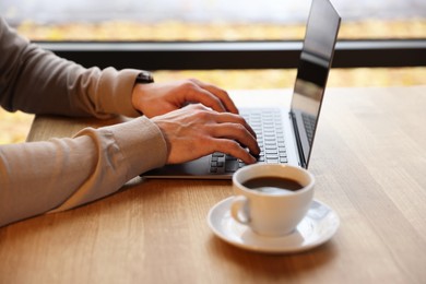 Photo of Man working on laptop at wooden table in cafe, closeup